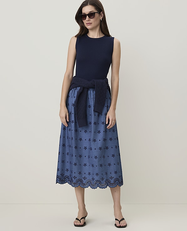 A woman in a navy ribbed tank top and a blue floral eyelet skirt stands against a plain, light-colored background.