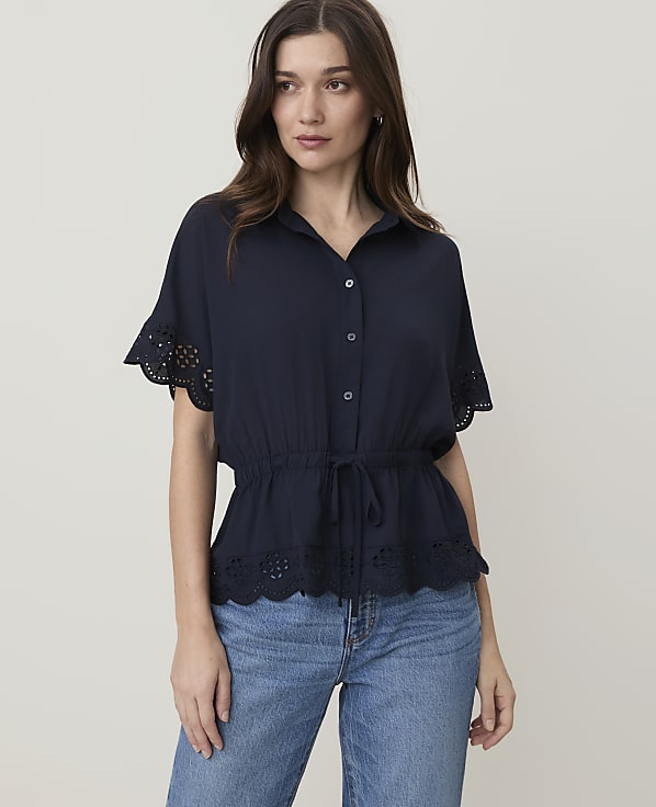 A woman in a navy blue blouse and jeans stands against a plain, light-colored background.