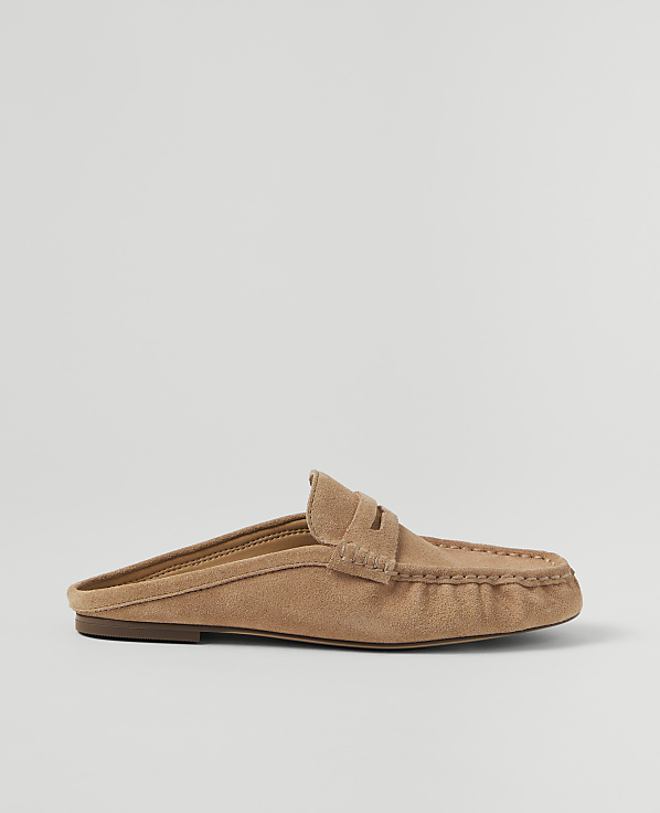 A tan suede mule loafer rests on a plain, light gray background.