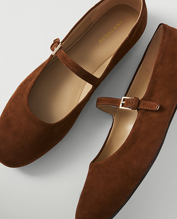 Two brown suede Mary Jane flats with gold buckles are arranged on a plain white background.