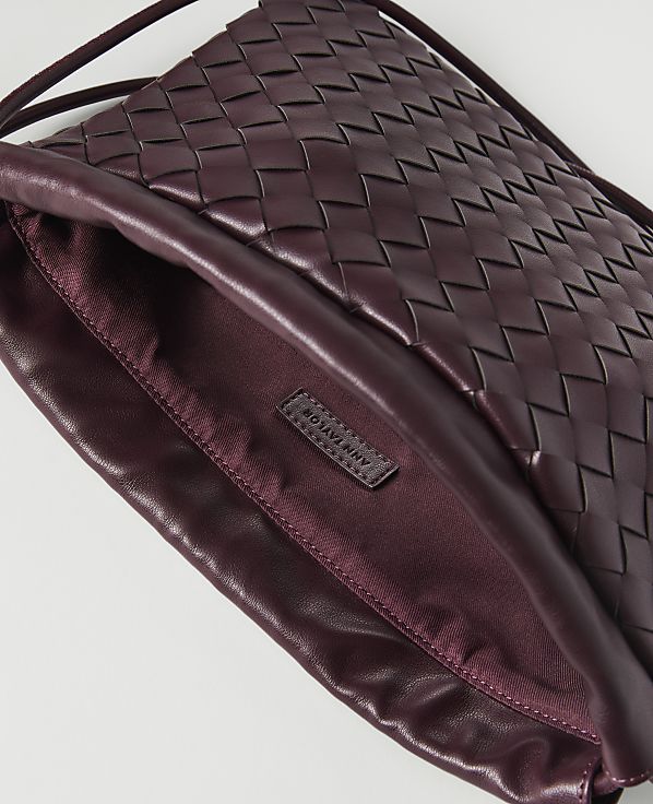 A woven burgundy leather clutch with a satin lining and a brand tag is shown against a white background.