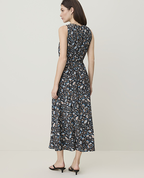 A woman in a floral print dress stands against a plain, light-colored background.