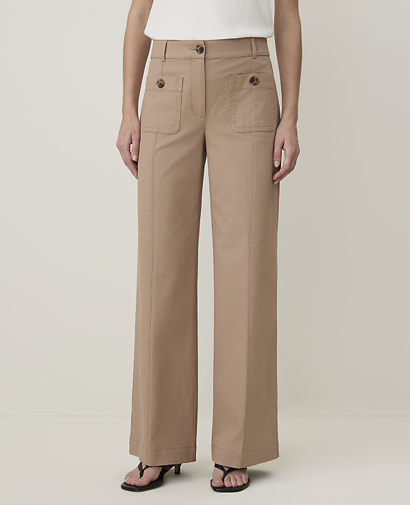 A person stands in front of a plain, light-colored background, wearing tan wide-leg pants with buttoned pockets and dark sandals.