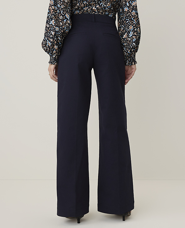 A person wearing a floral blouse and dark wide-leg pants stands against a plain, light-colored background.