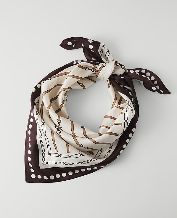 A silk scarf with a chain and polka dot pattern is laid out on a plain white background.