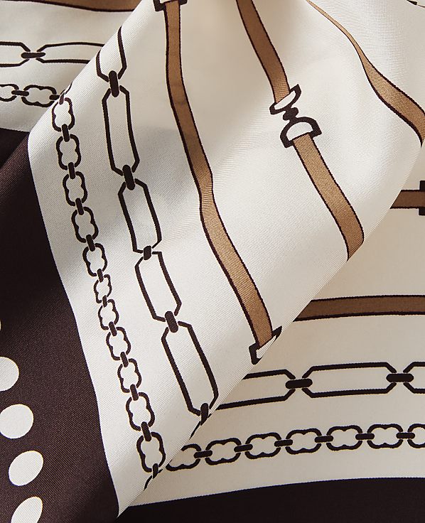 A cream-colored silk scarf with a brown chain and buckle pattern is folded in the foreground, with a plain cream background.