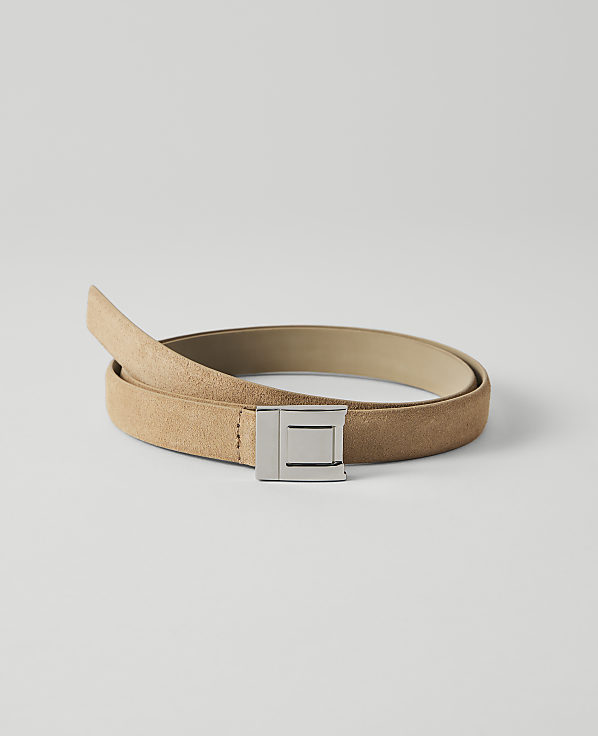A tan suede belt with a silver buckle lies coiled on a plain white background.