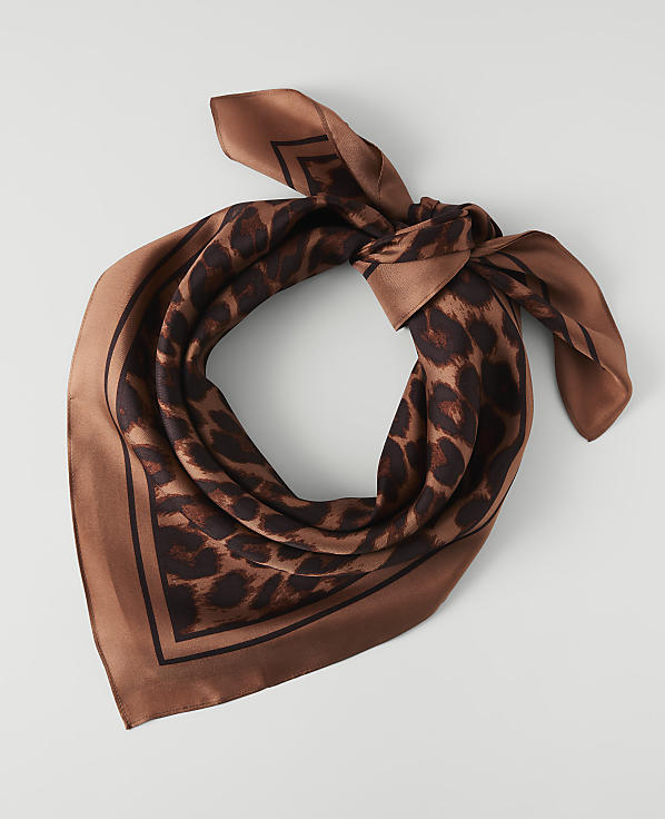 A brown leopard print silk scarf is tied in a knot in the foreground, against a plain white background.