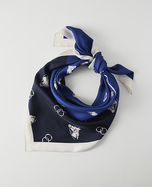A blue and white patterned silk scarf is tied in a knot against a plain white background.