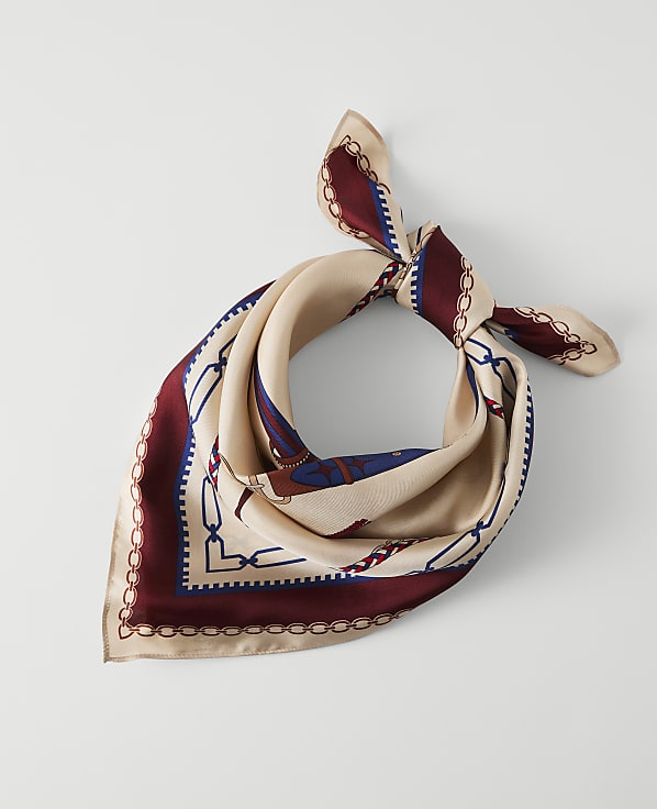 A cream-colored silk scarf with a maroon and blue chain link pattern is laid flat against a plain white background.