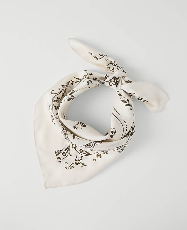 A cream-colored bandana with a dark floral pattern is tied in a knot against a plain white background.