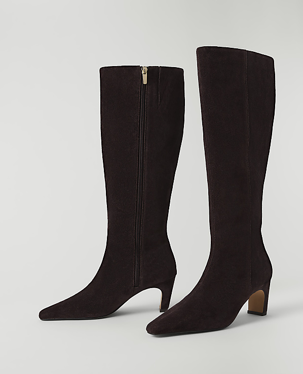 A pair of dark brown suede knee-high boots with a zipper detail stand on a plain white background.