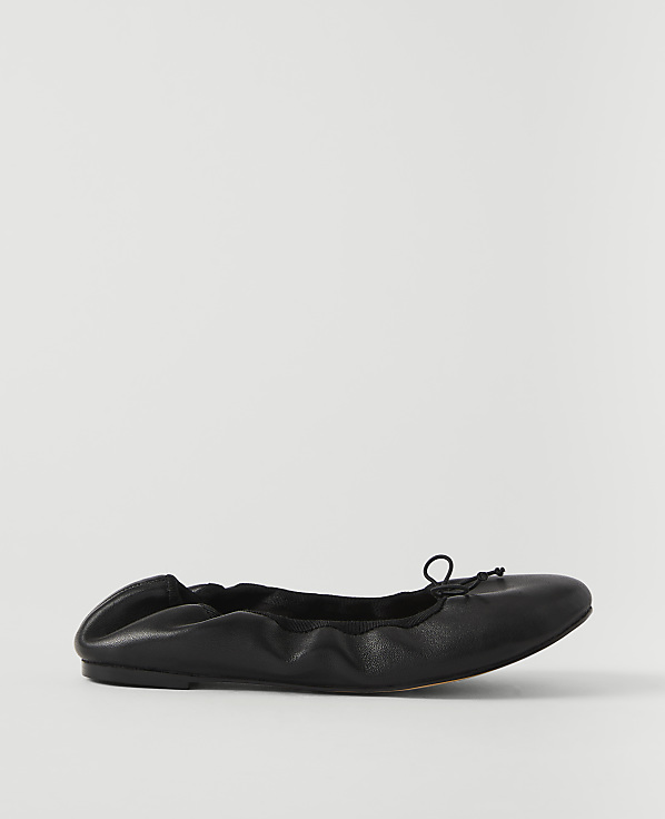 A black leather ballet flat with a drawstring bow rests on a plain white background.