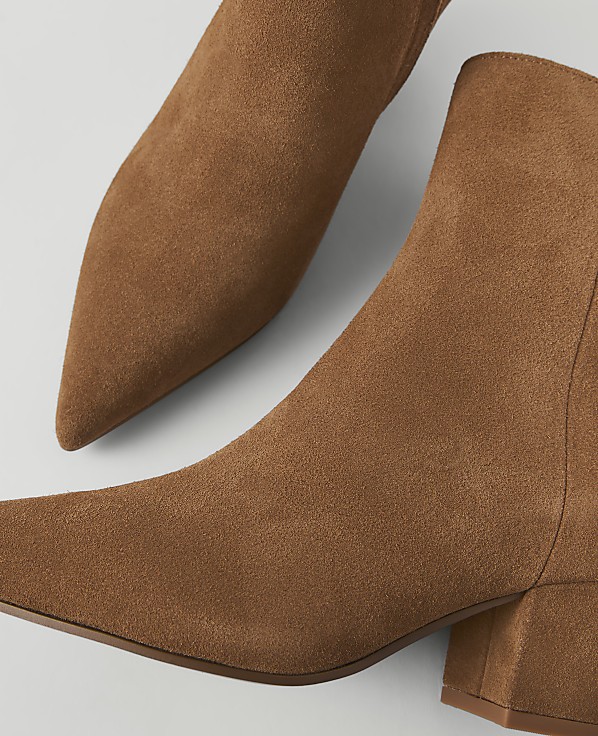 Two brown suede ankle boots with pointed toes and block heels are arranged on a white background.