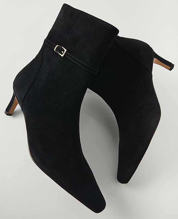 A pair of black suede ankle boots with a buckle detail are displayed against a plain white background.