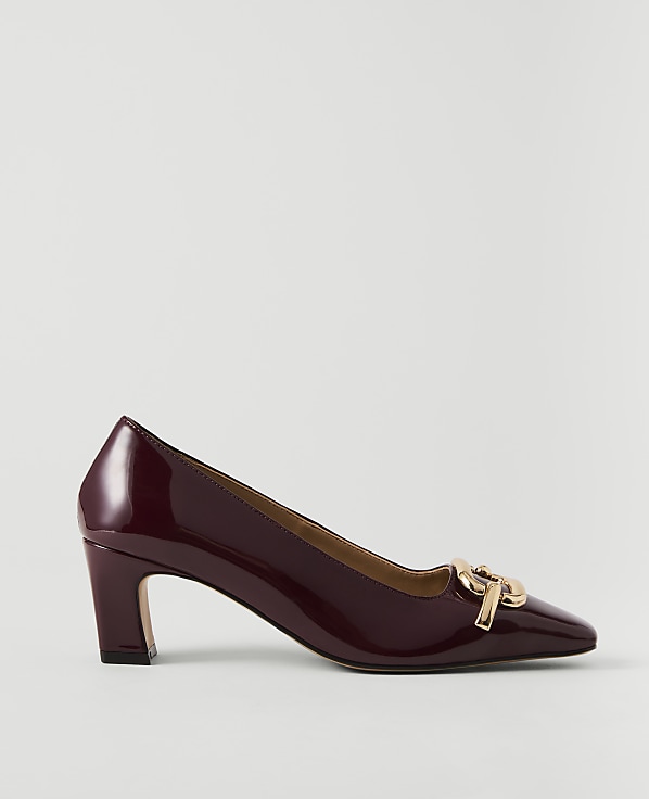 A glossy burgundy pump with a gold buckle sits on a plain white background.