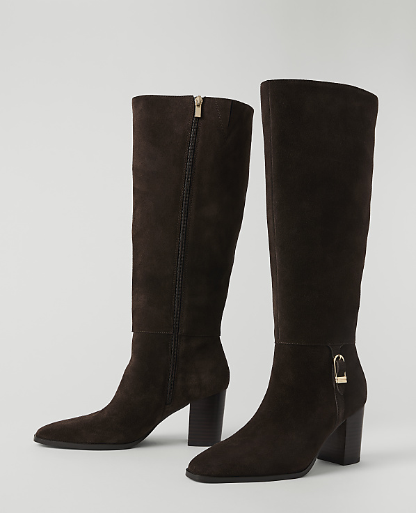 A pair of dark brown suede knee-high boots with gold accents stand on a plain white background.