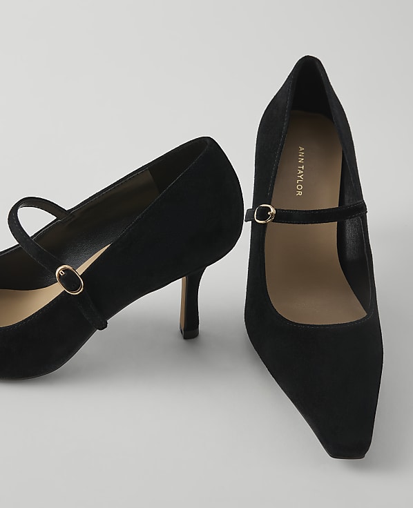 A pair of black suede Mary Jane heels with gold buckles rests on a plain white background.