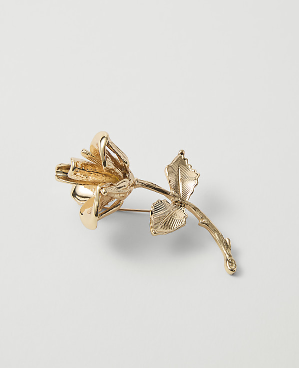 A golden rose brooch with detailed petals and leaves rests on a plain white background.