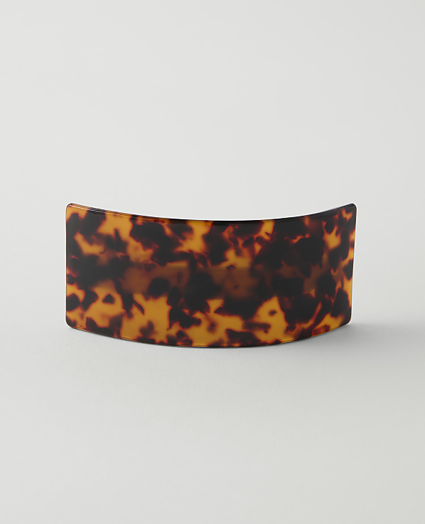 A tortoiseshell barrette with a curved shape rests on a plain white background.