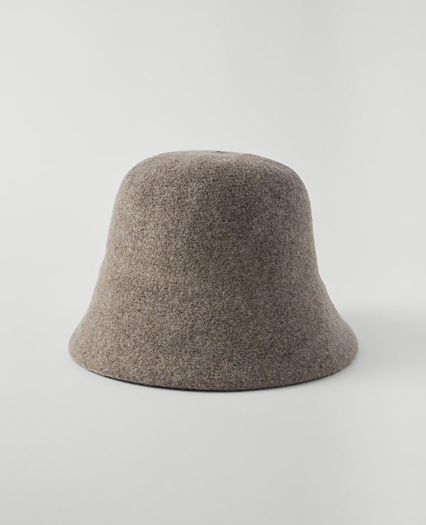 A fuzzy, taupe bucket hat sits centered on a plain, light gray background.