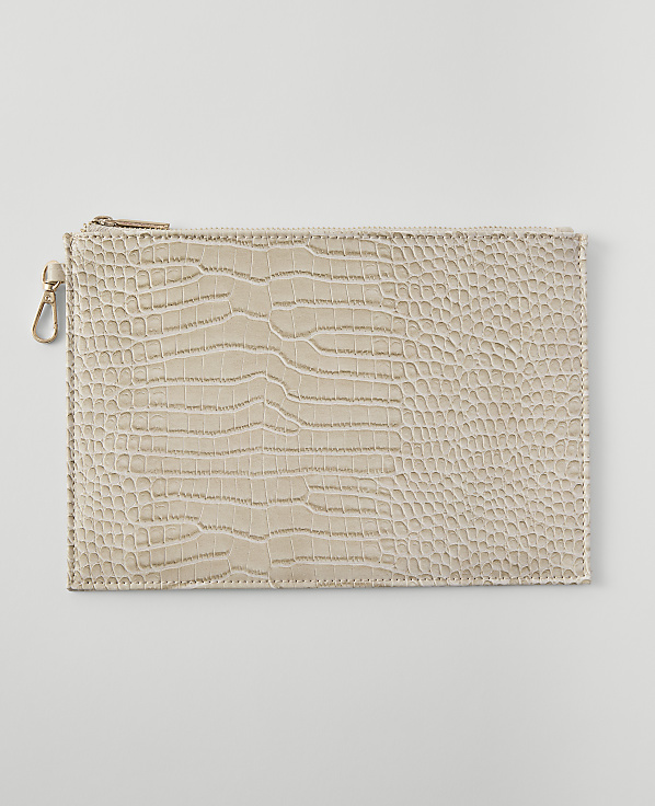 A beige, crocodile-embossed clutch with a gold zipper and clasp rests on a plain, light gray background.