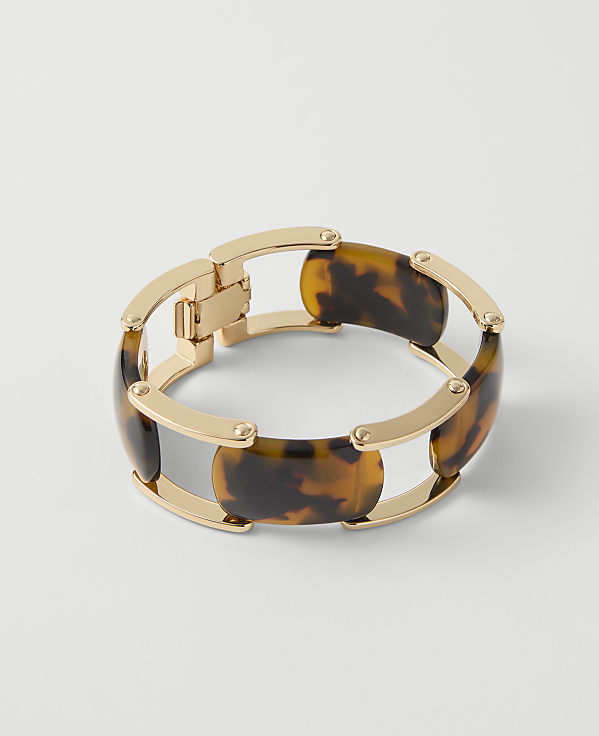 A gold and tortoiseshell bracelet rests on a plain white background.
