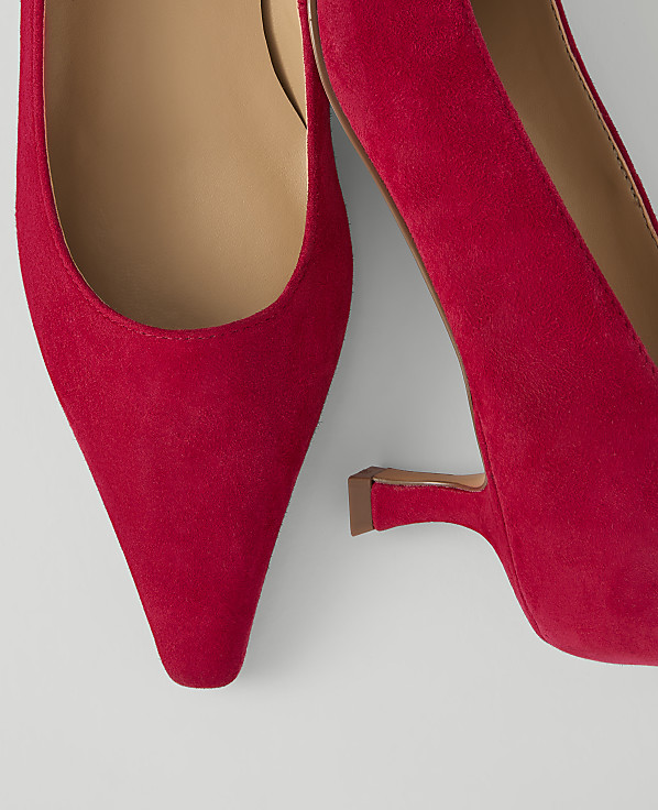 A close-up of two vibrant red suede pointed-toe heels with a light background.