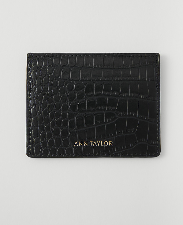 A black, crocodile-embossed cardholder with "ANN TAYLOR" in gold lettering rests on a plain white background.