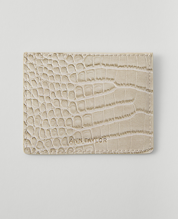 A light beige, crocodile-embossed wallet with "ANN TAYLOR" embossed on it rests on a plain white background.