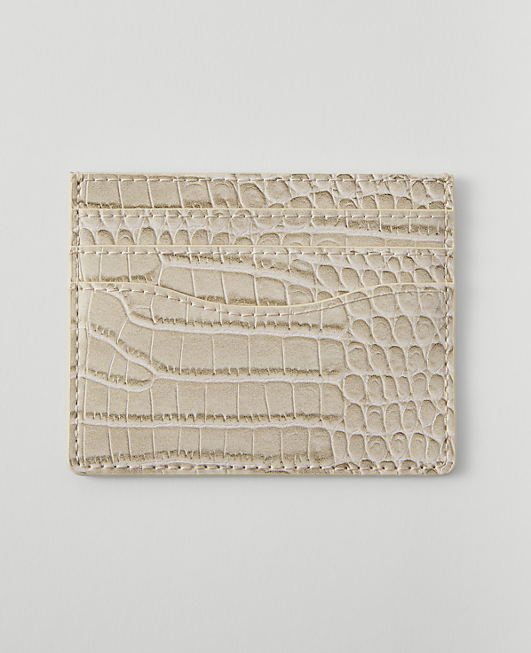 A light beige, crocodile-embossed cardholder with multiple slots rests on a plain white background.