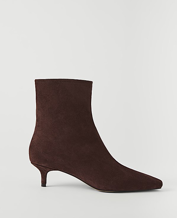 A brown suede ankle boot with a pointed toe and kitten heel stands against a plain white background.