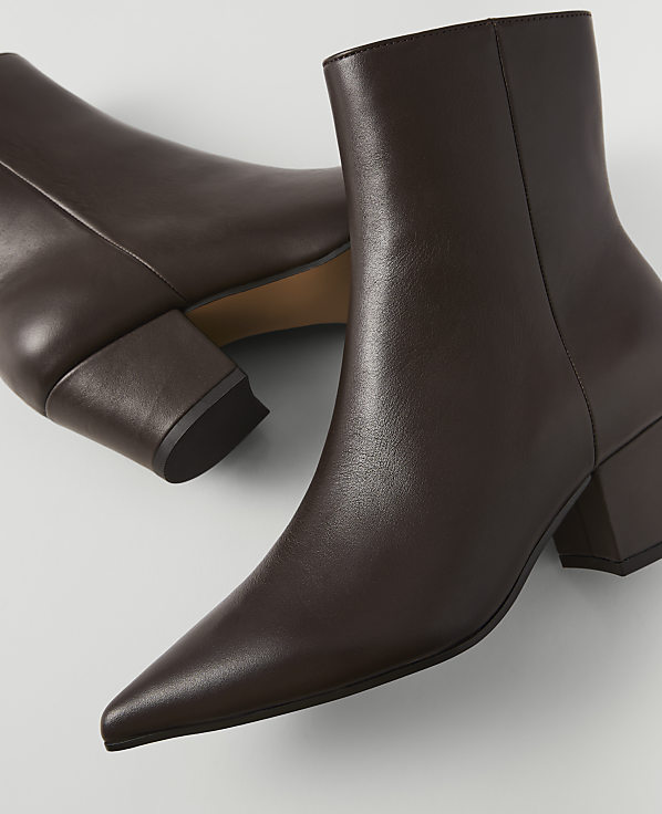 A pair of pointed-toe brown leather ankle boots with block heels rests on a light gray surface.