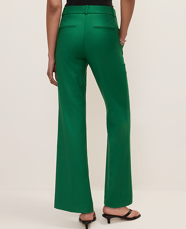 A person wearing bright green flared trousers and black heeled sandals stands against a plain, light-colored background.