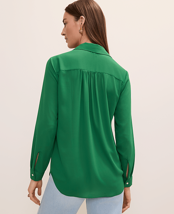 A woman in a green blouse and light blue jeans stands against a plain white background.