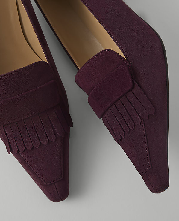 A pair of burgundy suede loafers with fringe detailing are displayed against a plain, light gray background.