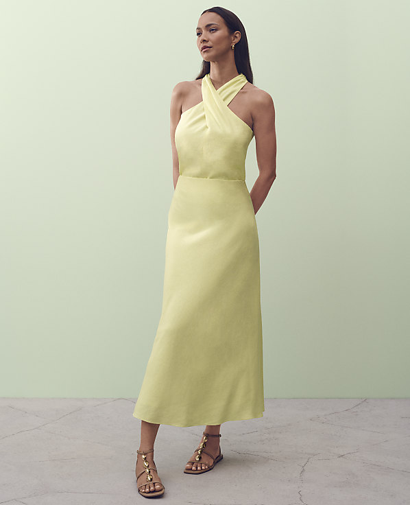 A woman in a pale yellow halter dress stands on a concrete floor against a pale green wall.