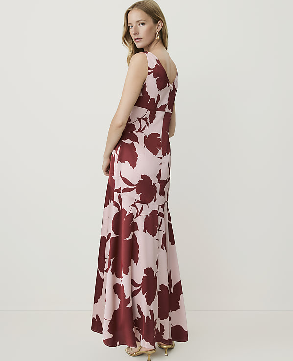 A woman in a floral maxi dress stands against a plain, light-colored background.