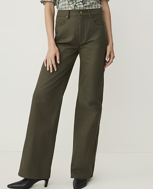 A person stands in olive green wide-leg pants and black pointed-toe heels against a plain white background.