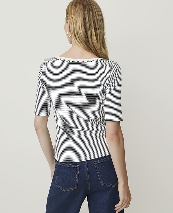 A woman in a striped shirt and jeans stands against a plain white background.