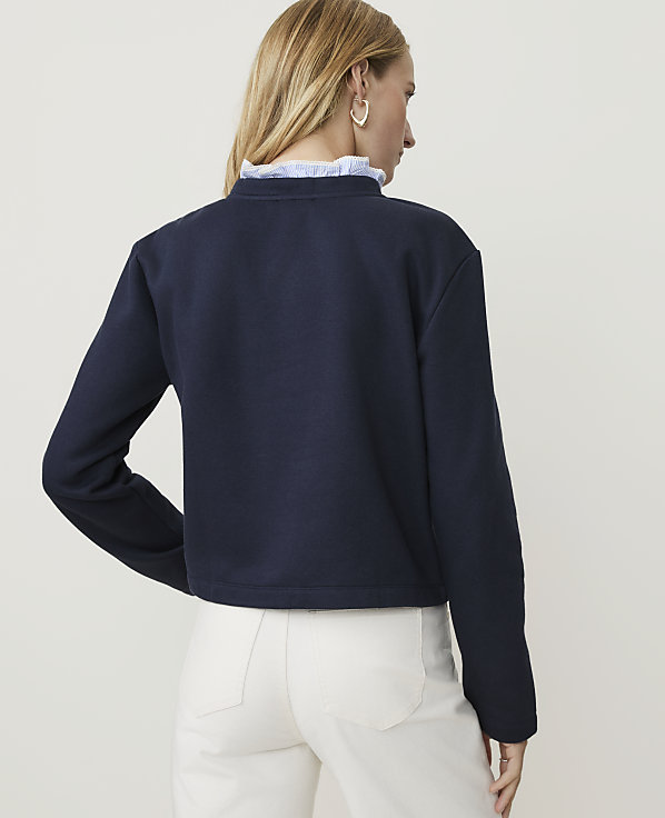 A woman in a navy sweatshirt and white pants stands against a plain white background.