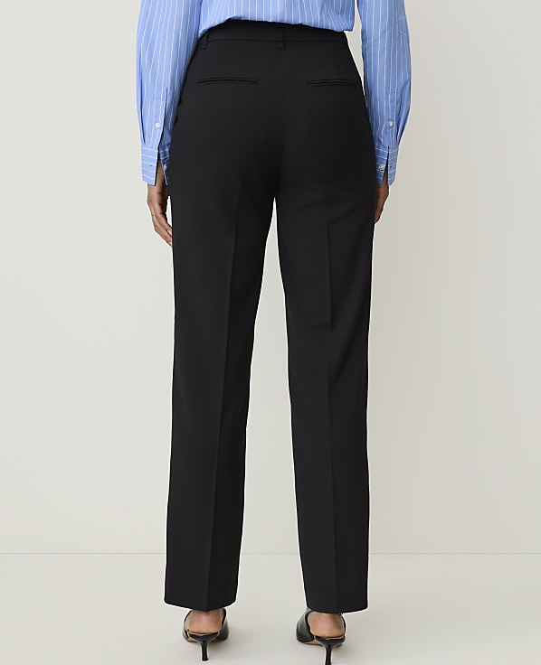 A person wearing black trousers and a blue striped shirt stands against a plain white background.