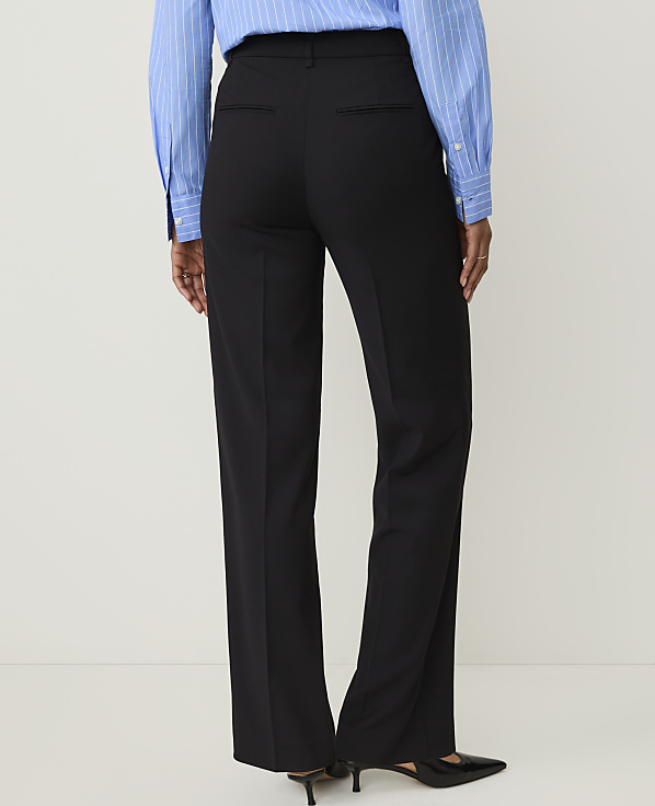 A person wearing black dress pants and a blue striped shirt stands against a plain white background.