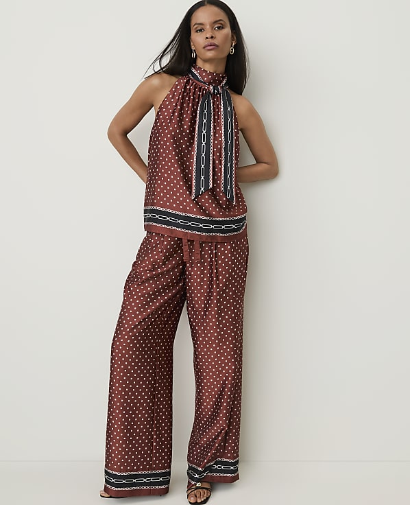 A woman in a patterned rust-colored halter top and wide-leg pants stands against a plain white wall.