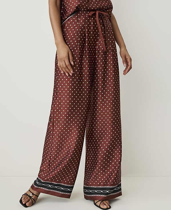 A person stands in wide-leg, patterned silk pants with a white background.