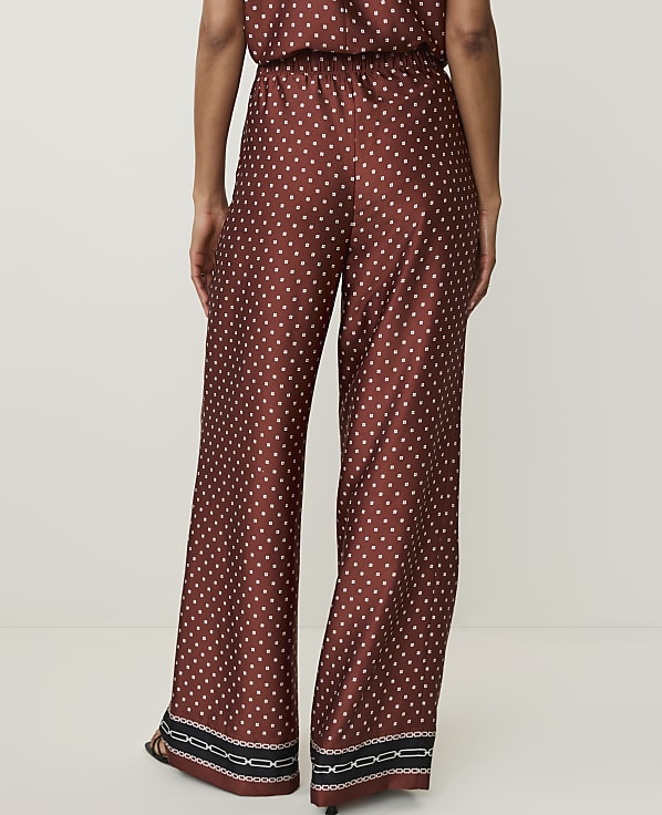 A person wearing patterned wide-leg pants stands against a plain white background.