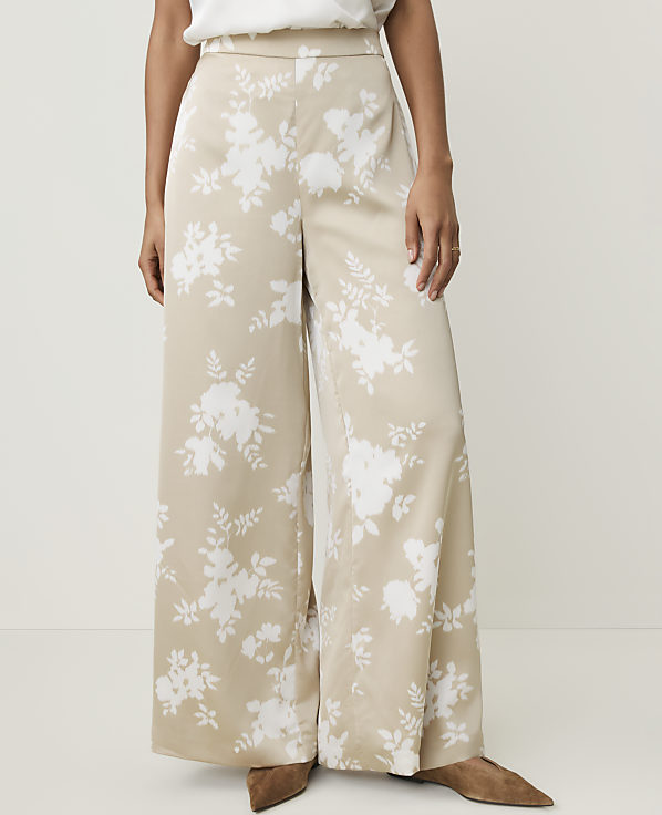 A person stands wearing wide-leg beige pants with a white floral pattern, against a plain white background.