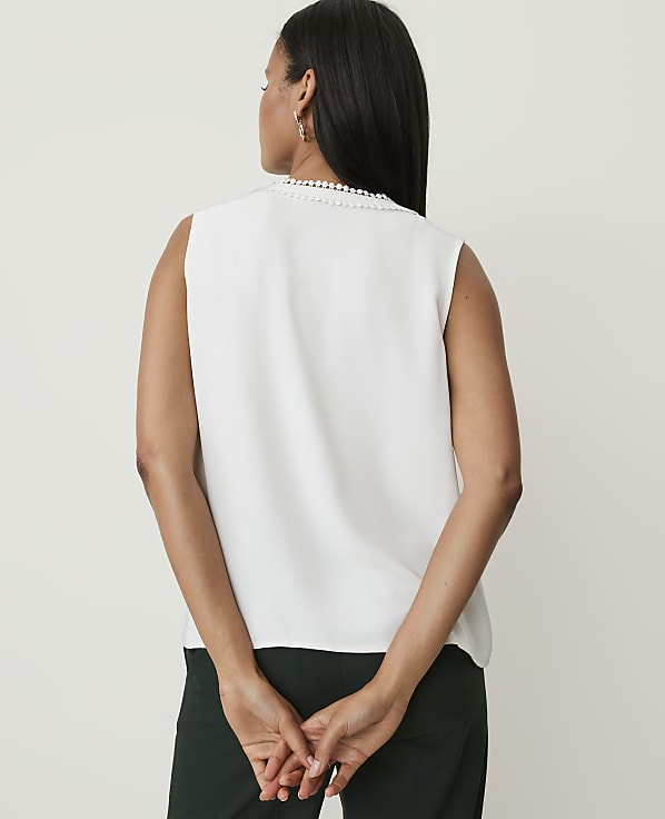 A woman in a white sleeveless top and dark green pants stands with her back to the camera against a plain white background.
