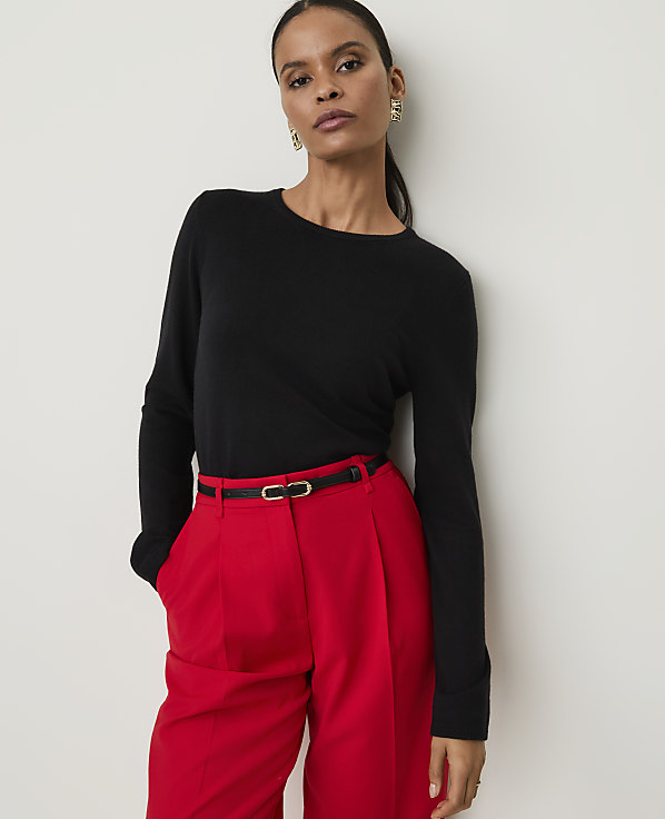 A woman in a black top and red pants stands against a plain white background.