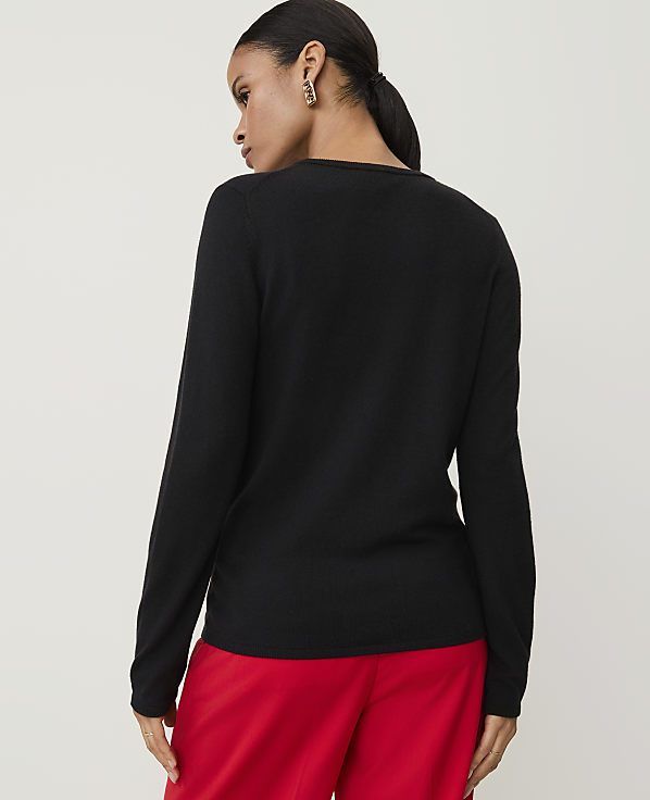 A woman in a black long-sleeved shirt and red pants stands against a plain white background.